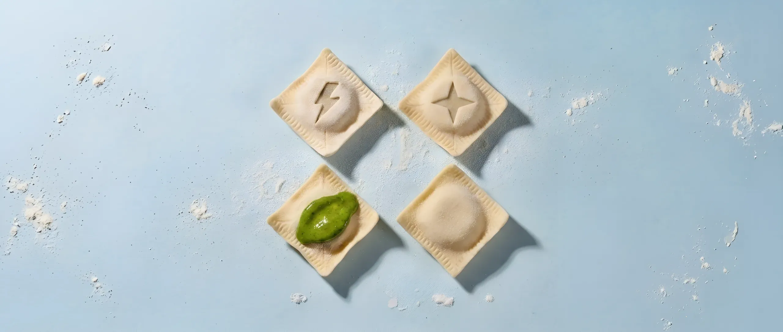 Four fresh ravioli flat on a pale blue studio field: a lightning bolt and a four-pointed spark carved into the dough of two, glossy pesto on a third, one plain